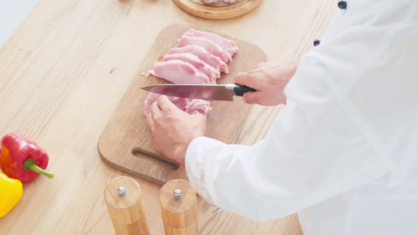 Vista ritagliata del filetto di maiale di taglio dello chef sul tagliere vicino alle verdure - Filmati, video