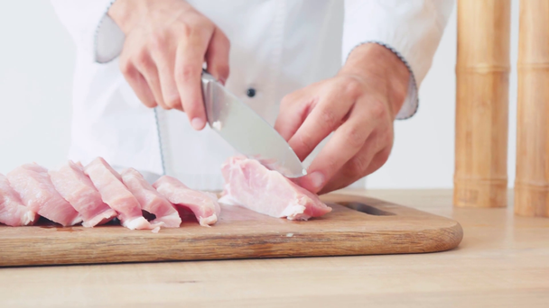 Vista cortada do chef cortando lombo de porco na tábua de corte no branco - Filmagem, Vídeo