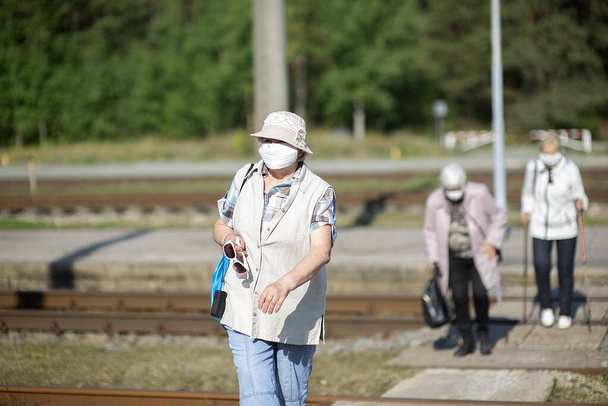 Eine Gruppe älterer Reisender mit Masken im Gesicht überquert die Bahngleise - Foto, Bild