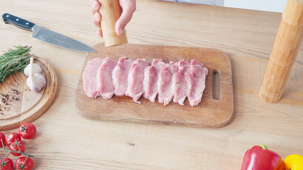 Geoogst uitzicht op chef-kok met molen kruiden plakken varkensvlees op snijplank - Video