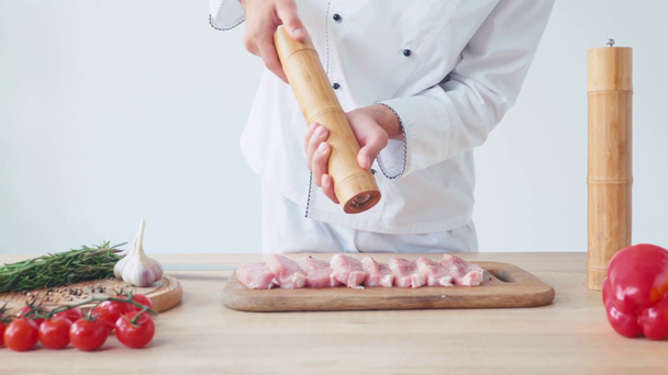 Обрезанный вид шеф-повара с соляной мельницей, приправляющий куски свиной вырезки на белом - Кадры, видео