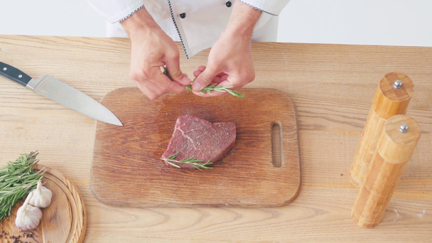 Vista ritagliata dello chef che mette rami di rosmarino sulla bistecca di manzo sul tagliere - Filmati, video