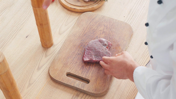 Vista cortada do chef com moinho tempero bife de carne na tábua de corte - Filmagem, Vídeo