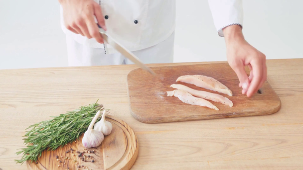 Καλλιεργημένη άποψη του σεφ κοπής φιλέτο κοτόπουλου σε λευκό φόντο στο τραπέζι - Πλάνα, βίντεο