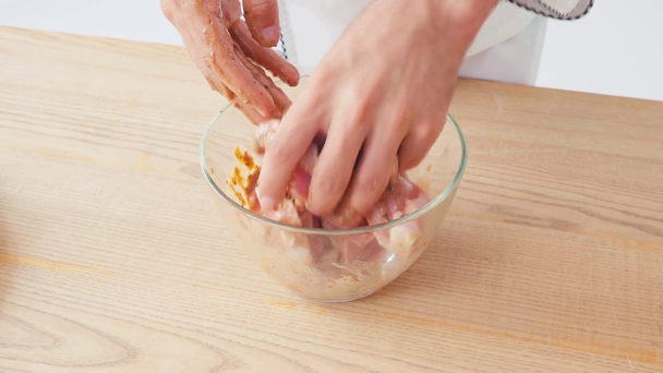 Vista recortada del chef marinando pollo en rodajas en un tazón sobre fondo blanco - Imágenes, Vídeo