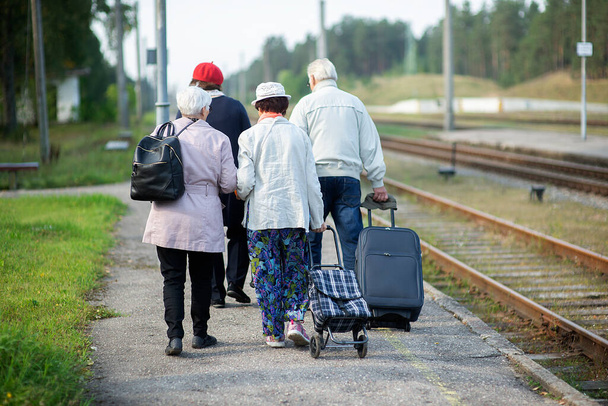 vista trasera de un grupo de ancianos ancianos ancianos con equipaje esperando un tren para viajar - Foto, imagen