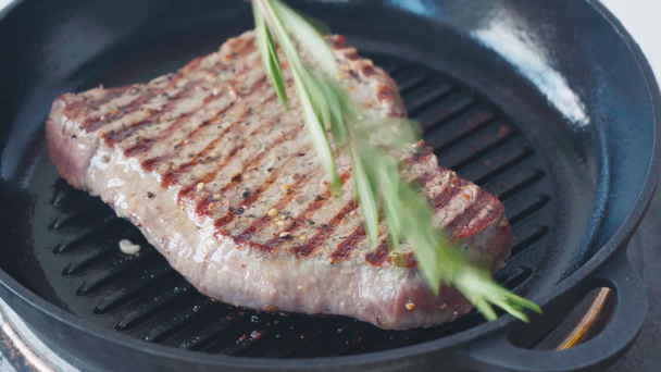 Close up widok szefa smarowania z rozmarynu smażona wołowina stek na patelni grill - Materiał filmowy, wideo
