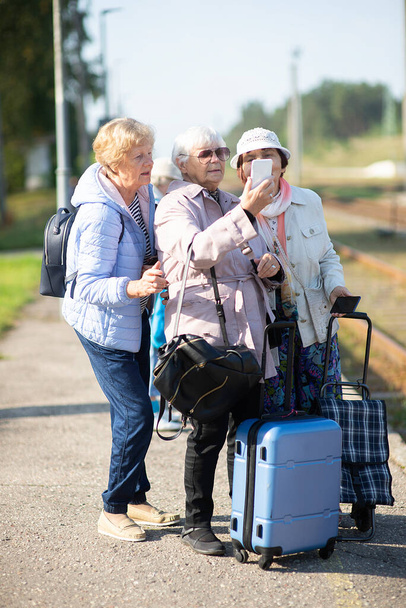 Mujeres mayores sonrientes toman un autorretrato en una plataforma esperando que un tren viaje durante una pandemia de COVID-19 - Foto, imagen