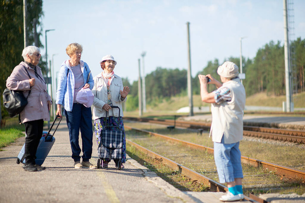 Usmívající se starší ženy vyfotí na nástupišti a čekají, až vlak pojede během pandemie COVID-19 - Fotografie, Obrázek