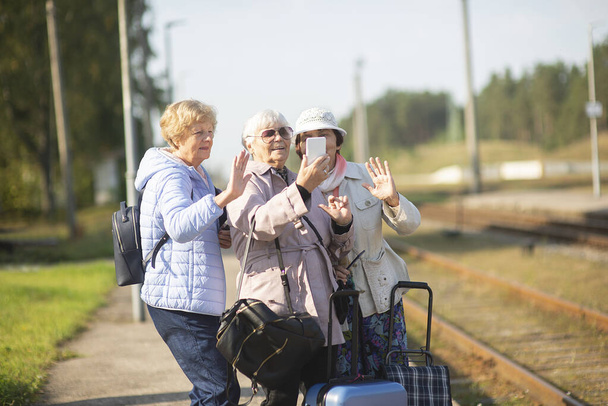 Grupo de mujeres mayores sonrientes toman un autorretrato en una plataforma esperando que un tren viaje durante una pandemia de COVID-19 - Foto, imagen