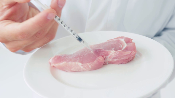 Обрезанный вид ученого, вводящего шприц в сырой кусок свинины на тарелке - Кадры, видео