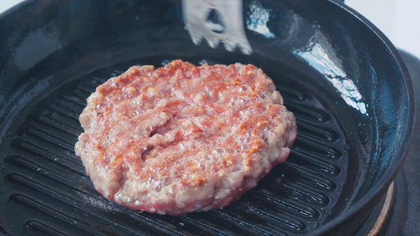 Close-up uitzicht op chef-kok met tang flipping rauwe kant van gehakt patty op hete pan - Video
