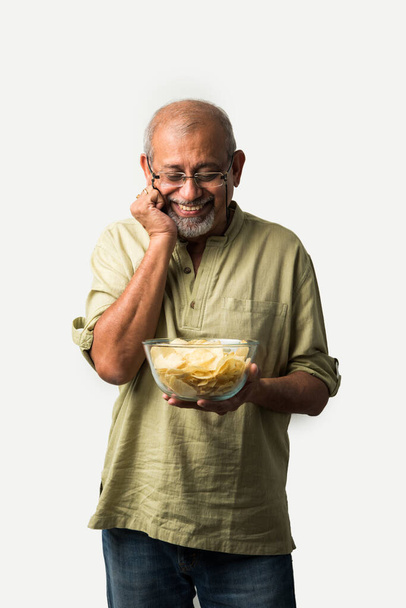 Індійський старий або пенсіонер, який їсть картопляні чіпси на білому фоні. - Фото, зображення