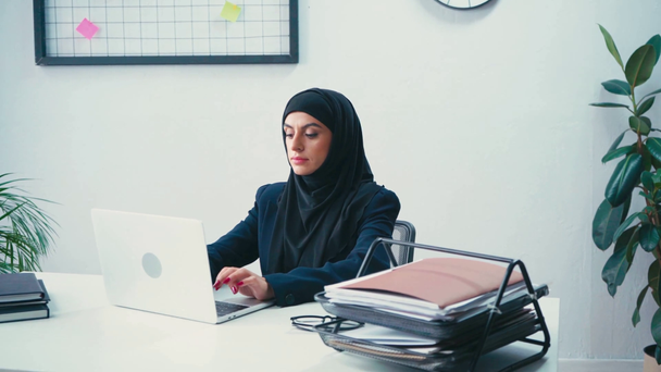 Mulher de negócios muçulmana usando laptop perto de papéis no escritório  - Filmagem, Vídeo