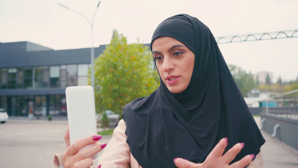 Joven mujer musulmana teniendo videollamada mientras camina por la calle urbana  - Imágenes, Vídeo