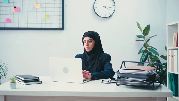 Muslimi liikenainen työskentelee kannettavan tietokoneen lähellä älypuhelin ja paperit toimistossa  - Materiaali, video