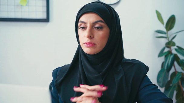 Smiling muslim businesswoman having video chat on laptop on blurred foreground - Video, Çekim
