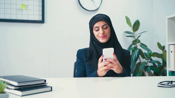 Muslimische Geschäftsfrau nutzt Smartphone in der Nähe von Papieren auf dem Tisch  - Filmmaterial, Video
