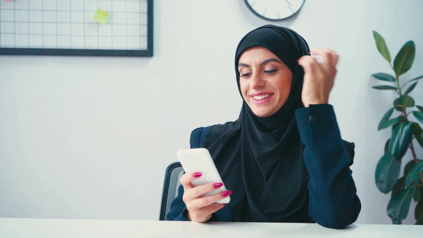 Sorridente donna d'affari musulmana utilizzando smartphone in ufficio  - Filmati, video