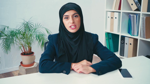 Muslim businesswoman waving and talking at camera near smartphone  - Video, Çekim