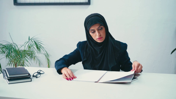 Muslimische Geschäftsfrau arbeitet mit Papieren in der Nähe von Smartphones und Notebooks - Filmmaterial, Video