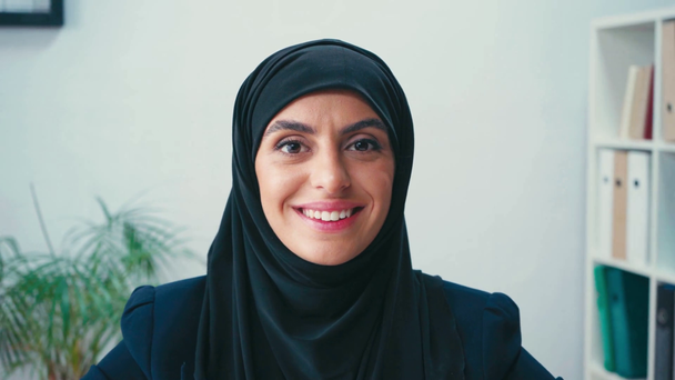 Donna d'affari musulmana sorridente alla macchina fotografica in ufficio  - Filmati, video
