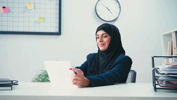 Мусульманська бізнес-леді за допомогою цифрового планшета поруч з паперами  - Кадри, відео