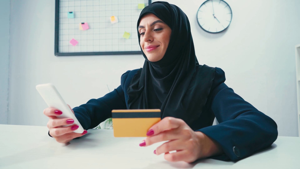 Femme d'affaires musulmane souriant tout en utilisant smartphone et carte de crédit  - Séquence, vidéo