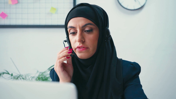 Empresaria musulmana con auriculares y portátil en primer plano borroso  - Imágenes, Vídeo
