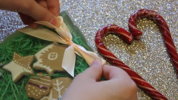 Weibliche Hände binden Geschenkschleifen an eine Geschenkschachtel mit Ingwerkeksen. Weihnachtsgeschenk - Filmmaterial, Video