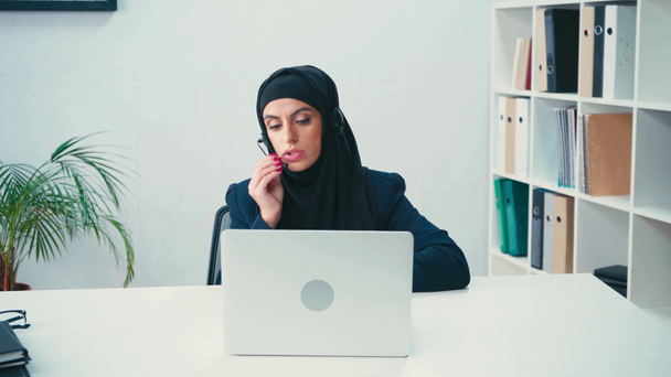 Мусульманская деловая женщина разговаривает на наушниках и с помощью ноутбука в офисе  - Кадры, видео