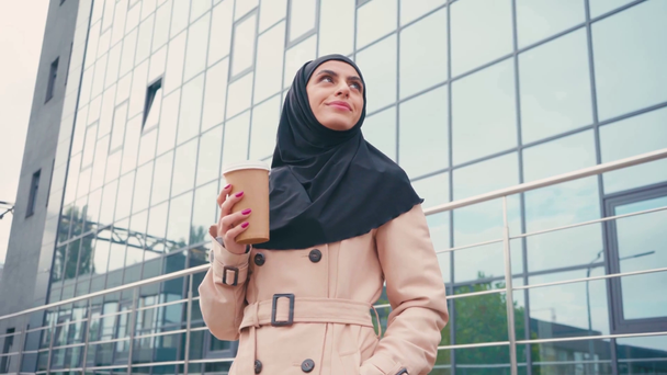 Donna musulmana in hijab bere caffè per andare vicino edificio  - Filmati, video