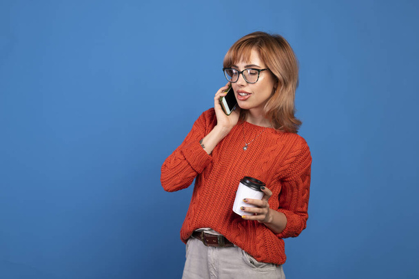 Retrato de una joven mujer casual sonriente hablando por teléfono móvil aislado sobre fondo azul. - Foto, imagen