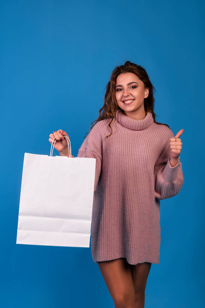 Beautiful asian young irl holding a white blank paper bag and makes purchases in an online store against a black wall background with copy space for text or design. Horizontal mockup - Photo, image