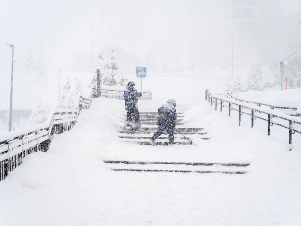 Workers clear snow on steps during heavy snowfall on a foggy day - Photo, Image
