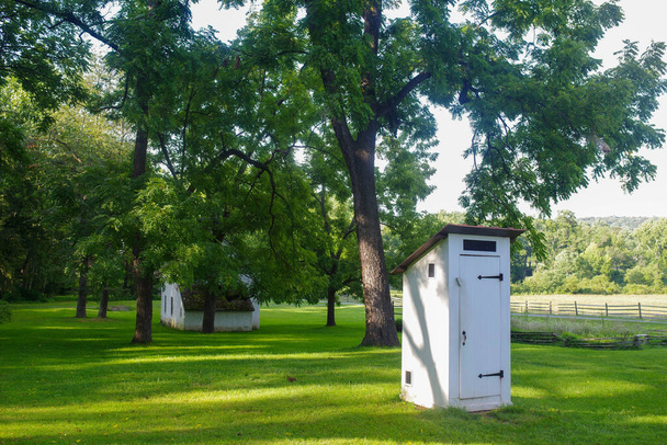 Колониальный туалет по каменному коттеджу, зеленой траве и деревьям. - Фото, изображение
