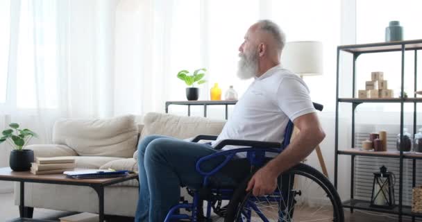 Zdravotně postižený starší muž sedí doma na invalidním vozíku - Záběry, video