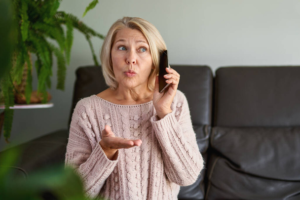idős nő egy telefonhívásban ül egy kanapén a nappaliban egy házban - Fotó, kép