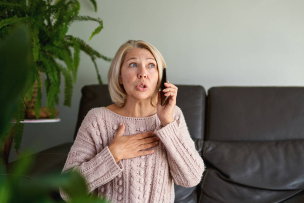 senior woman in a phone call sitting on a sofa in the living room in a house - Photo, Image