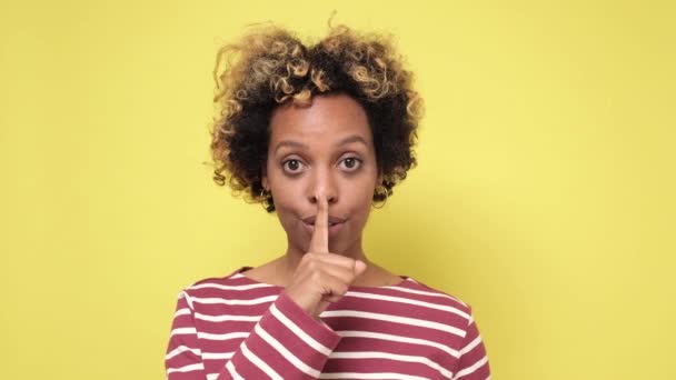 Hübsche junge Afroamerikanerin macht Schweigegegeste, drückt Zeigefinger an Lippen. - Filmmaterial, Video