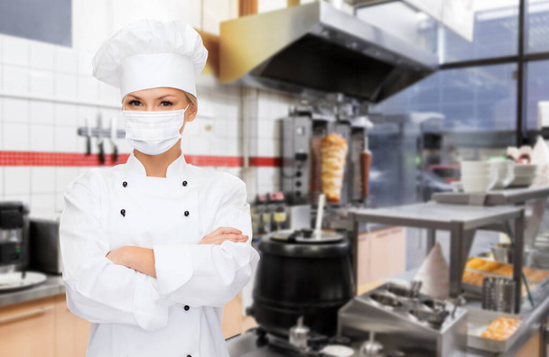 female chef in mask with crossed arms at kitchen - Фото, изображение