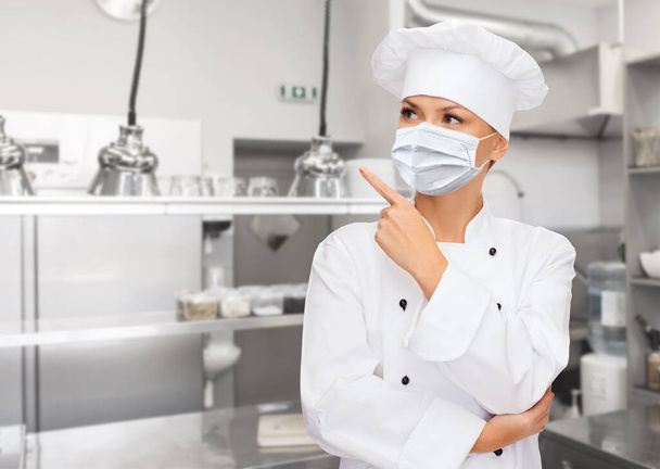 female chef in mask pointing finger up at kitchen - Foto, Imagem