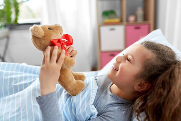 happy little girl with teddy bear lying in bed - Фото, зображення