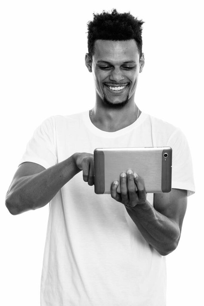 若い幸せなアフリカ人男性のスタジオショットは、デジタルタブレットを使用して笑顔 - 写真・画像
