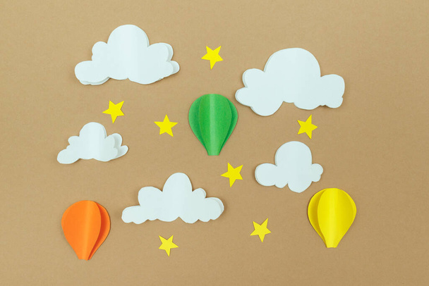 Σύννεφα από χαρτόνι, αστέρια και αερόστατα στο μπεζ φόντο. Μπαλόνια στον ουρανό με αστέρια και σύννεφα. - Φωτογραφία, εικόνα