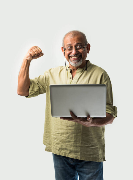 Indiano asiatico anziano adulto uomo o nonno utilizzando laptop e in possesso di banconote di carta contro sfondo bianco - Foto, immagini