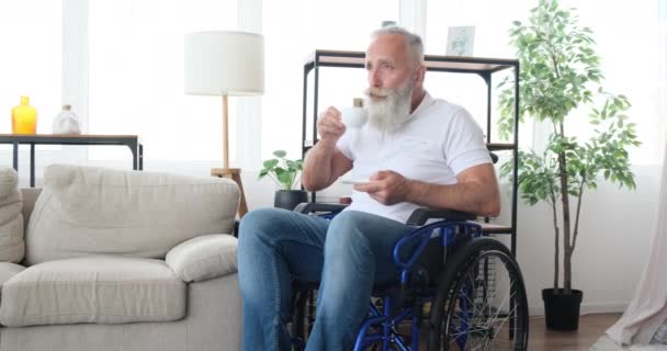 Vecchio con disabilità bere caffè seduto sulla sedia a rotelle - Filmati, video