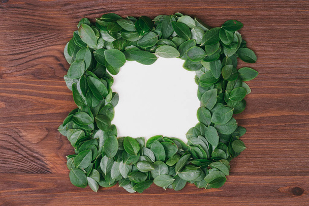 Creative frame made of  leaves with paper card note on a wood background. Flat lay. Nature concept.Top view.  Blank for advertising card or invitation.  - Φωτογραφία, εικόνα
