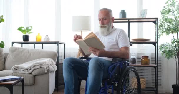 Senior man with disability reading a book sitting on wheelchair - Footage, Video