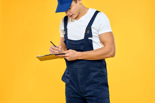 Чоловік у робочій уніформі документи надання послуг жовтий фон
 - Фото, зображення